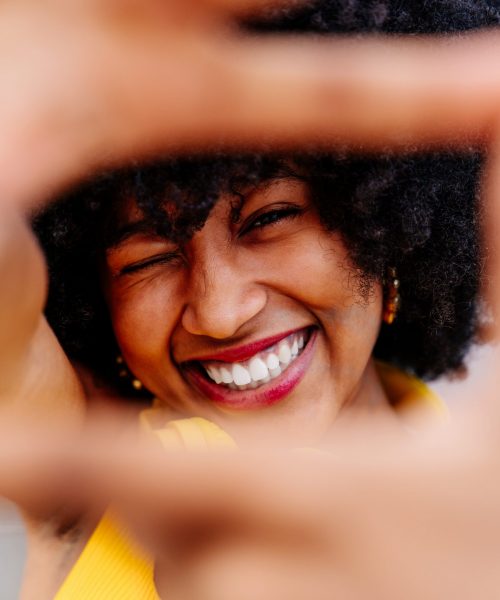 Beautiful young happy african woman with afro curly hairstyle strolling in the city - Cheerful black student portrait on colorful wall background