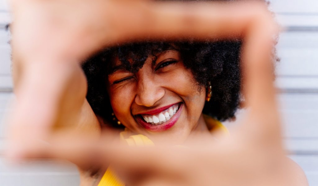 Beautiful young happy african woman with afro curly hairstyle strolling in the city - Cheerful black student portrait on colorful wall background