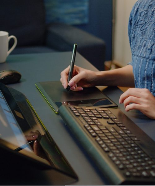 Close up of photo editing equipment at photography studio on desk. Woman working as editor using retouching software, keyboard and graphic tablet with stylus for retouch media project