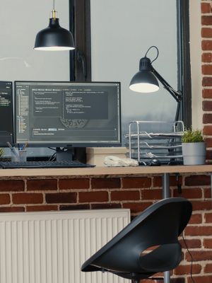 Desk with multiple computer monitors displaying parsing code and programming language compiling in empty software developing agency office. Servers cloud computing big data algorithms.